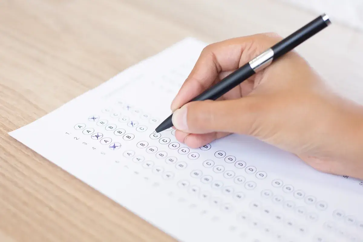 A hand filling in a multiple-choice answer sheet with a pen