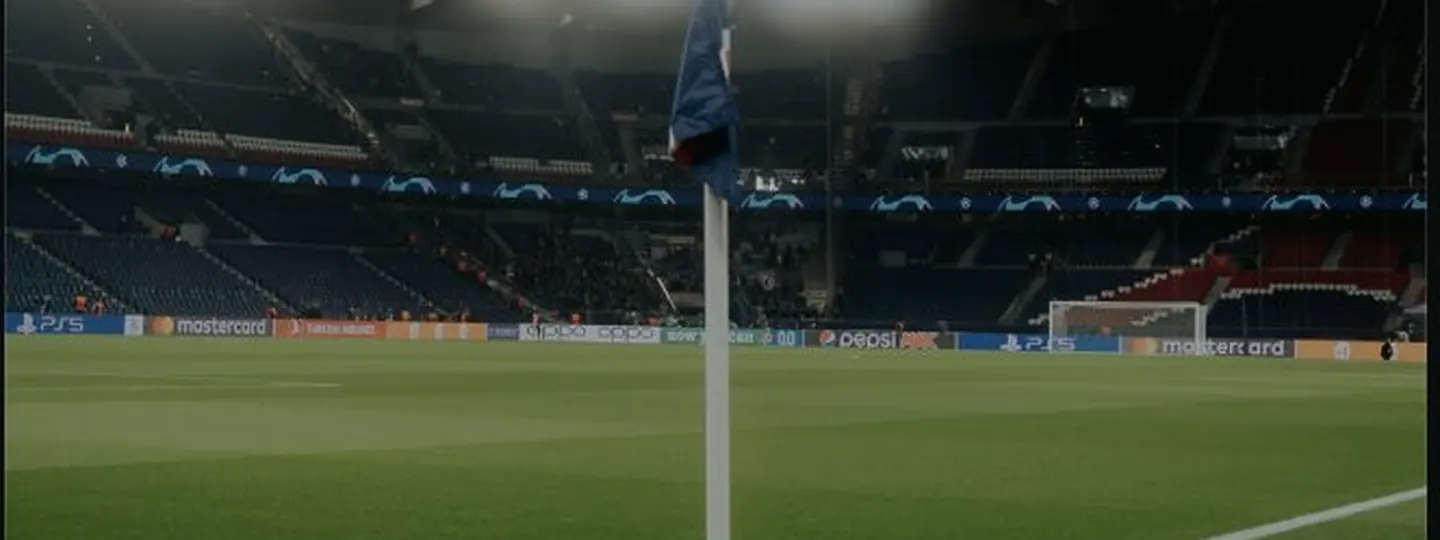 Un drapeau de corner au premier plan, devant des tribunes plongées dans la pénombre et un terrain éclairé par les projecteurs