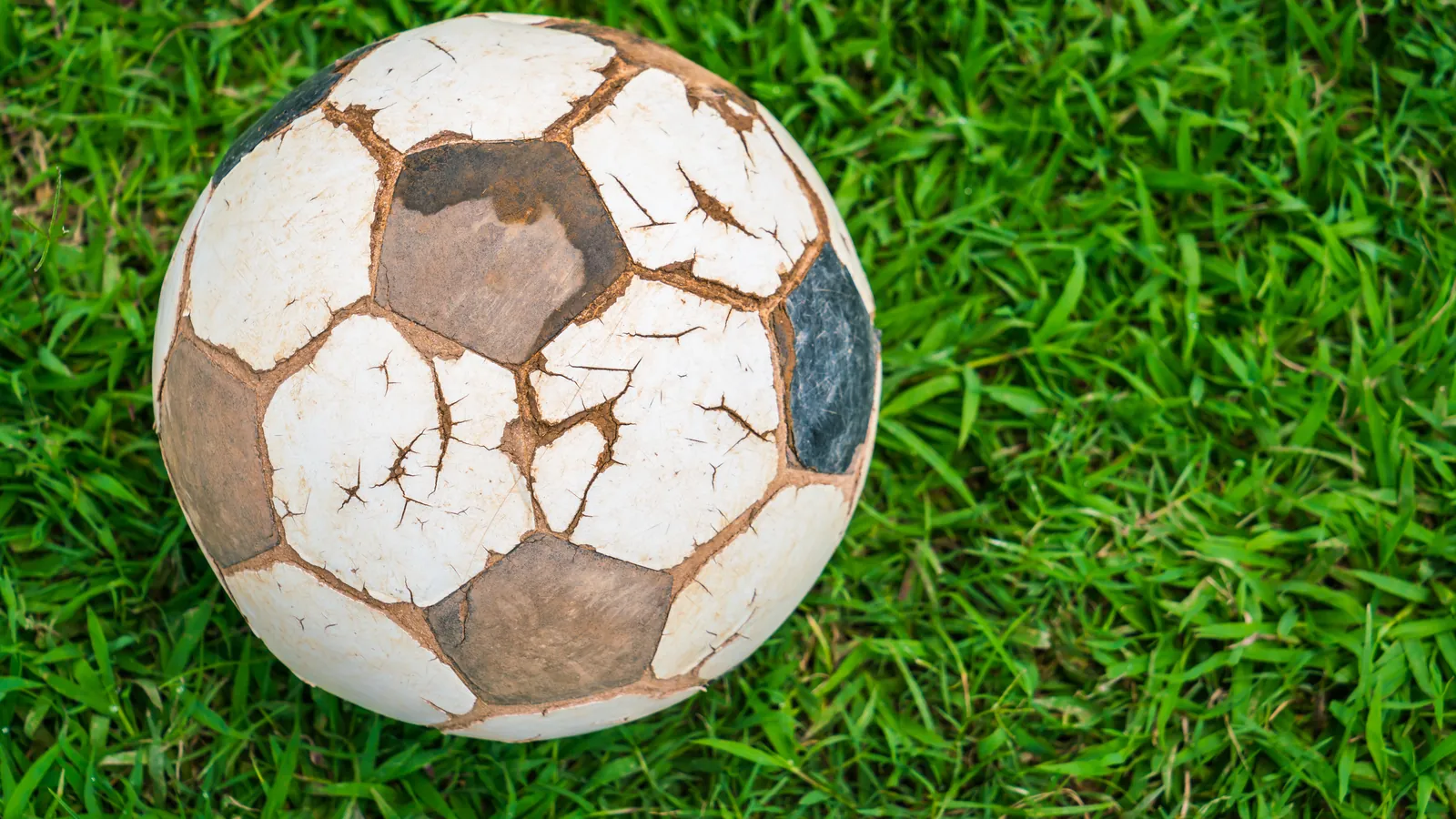 Un vieux ballon de football en cuir, usé et craquelé, posé dans l'herbe