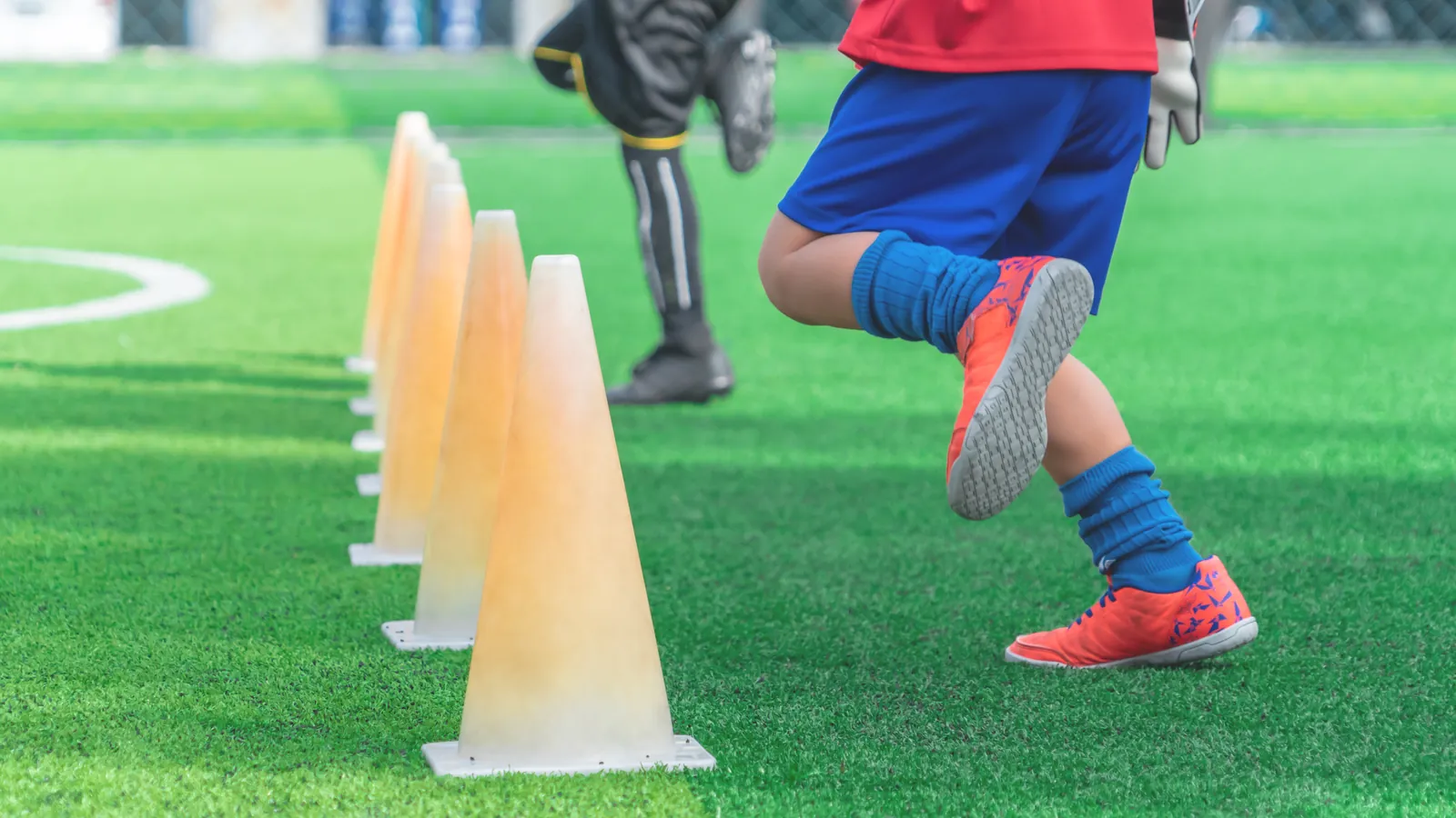 Les jambes d'un jeune joueur en crampons à côté de plots d'entraînement, sur un terrain synthétique