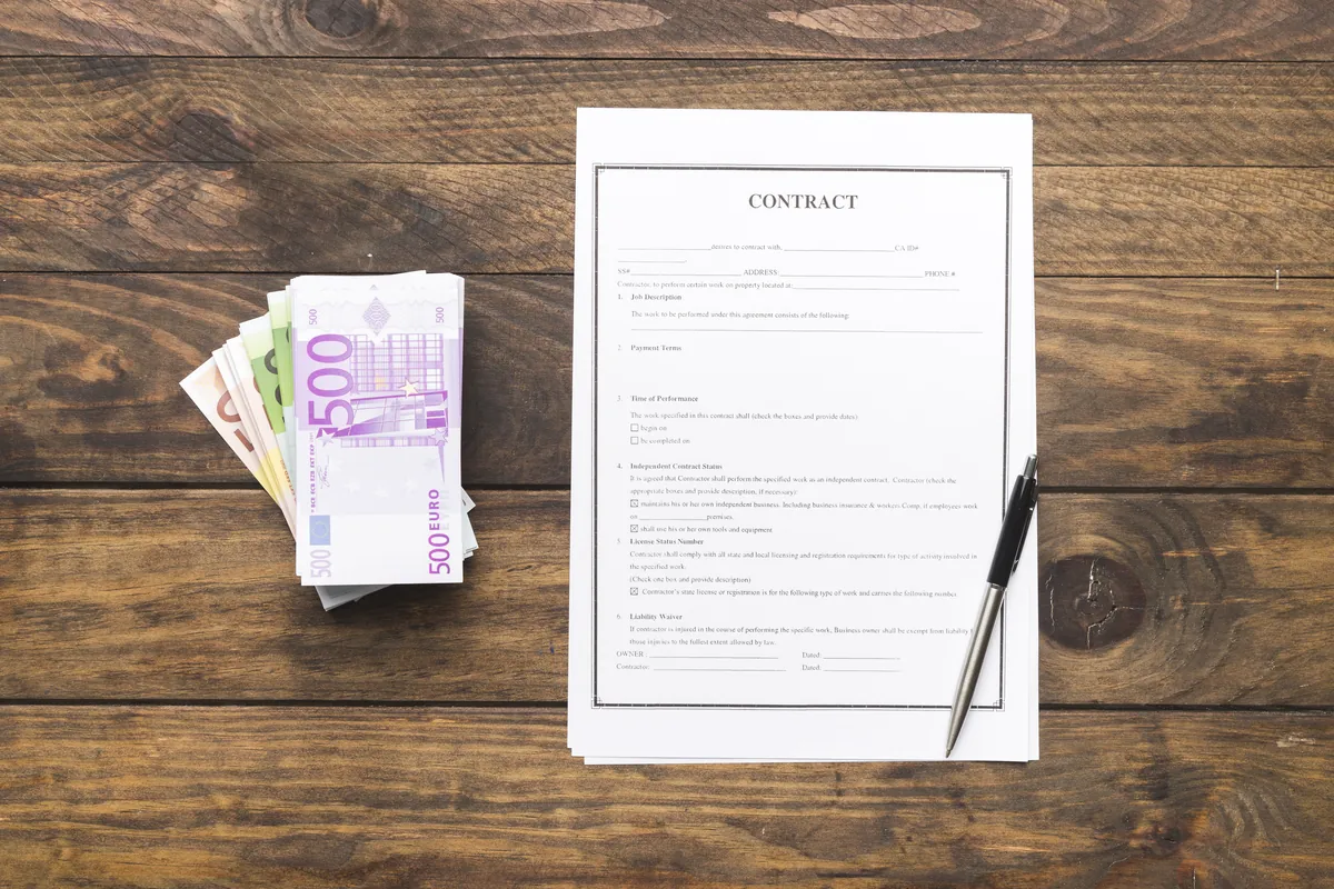 Un contrat, un stylo et une liasse de billets en euros sur une table en bois