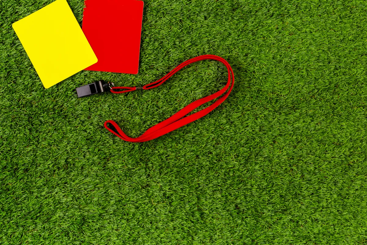 Un carton jaune, un carton rouge et un sifflet posés sur une pelouse