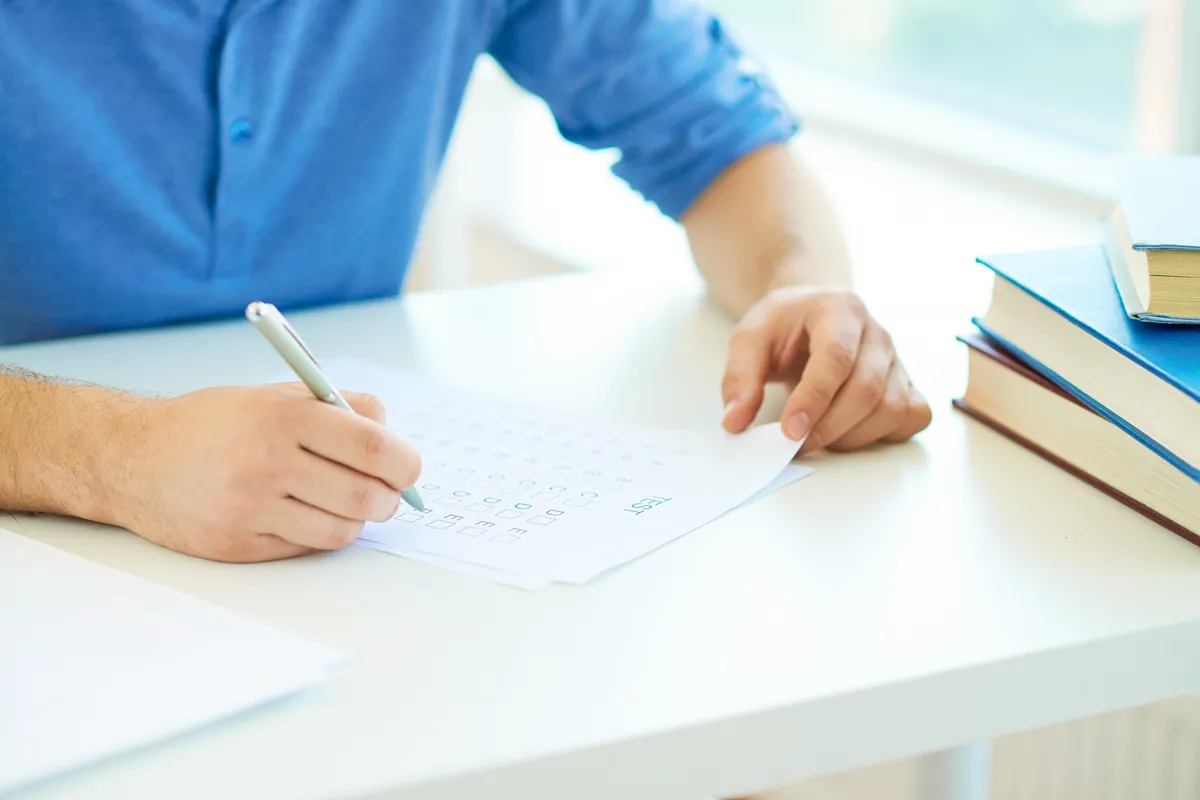 Un candidat rédige sa copie d'examen à un bureau, à côté d'une pile de livres