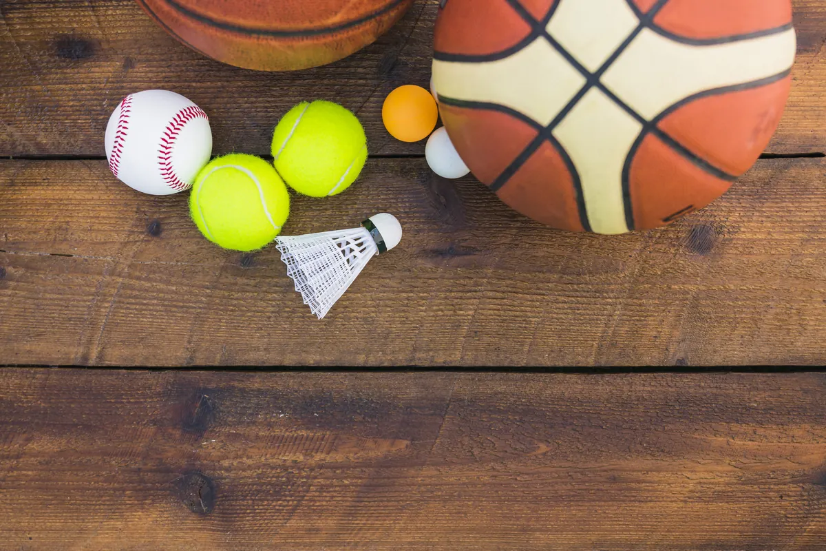 Une balle de tennis, un volant, une balle de baseball et un ballon de basket sur un plancher en bois