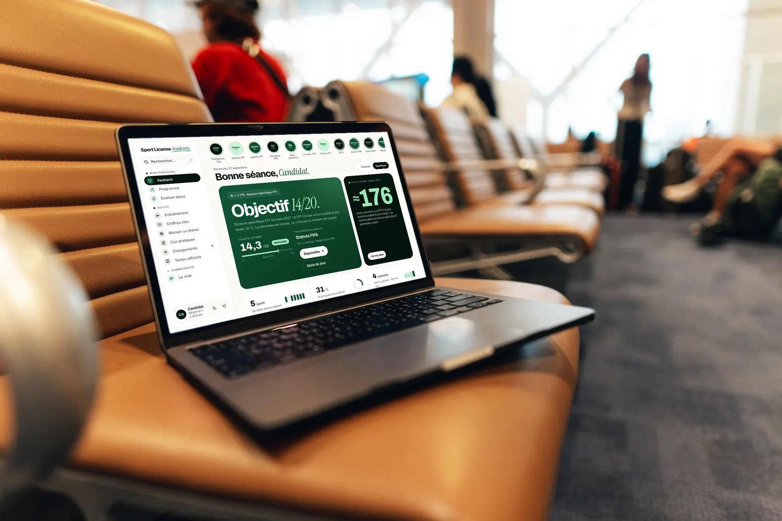 Un ordinateur portable ouvert sur le tableau de bord de Sport License Academy, posé sur un siège en cuir fauve dans une salle d'embarquement d'aéroport, avec des voyageurs flous en arrière-plan